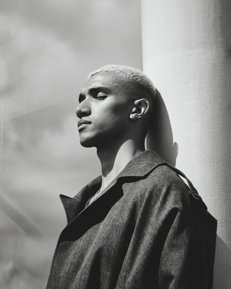 Monochrome side view shot of stylish young man leaning against column