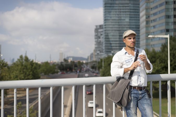 Confident male in denim with city in background closing water bottle top, copy space