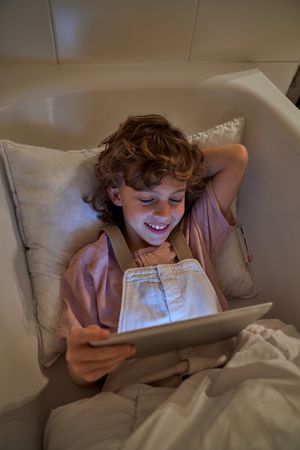 Happy boy browsing tablet in bathtub