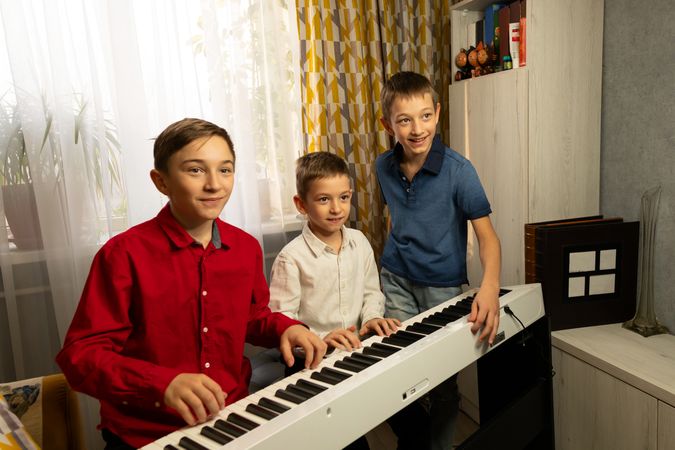 Three boys gathered around piano, enjoying music together