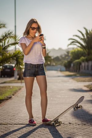 Young girl with a skateboard using the smartphone outdoor