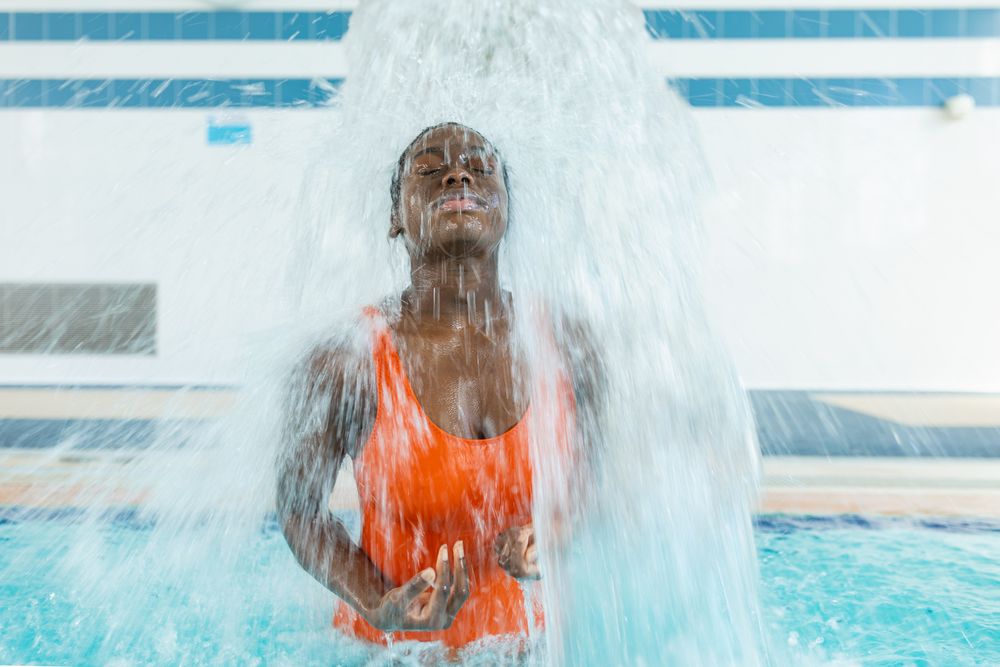 Black young woman massaging her back under a water jet at the swimming pool