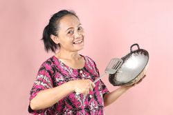 Indonesian Mom Holding Cooking Appliance, Wajan Frying Pan and Slotted Spatula.