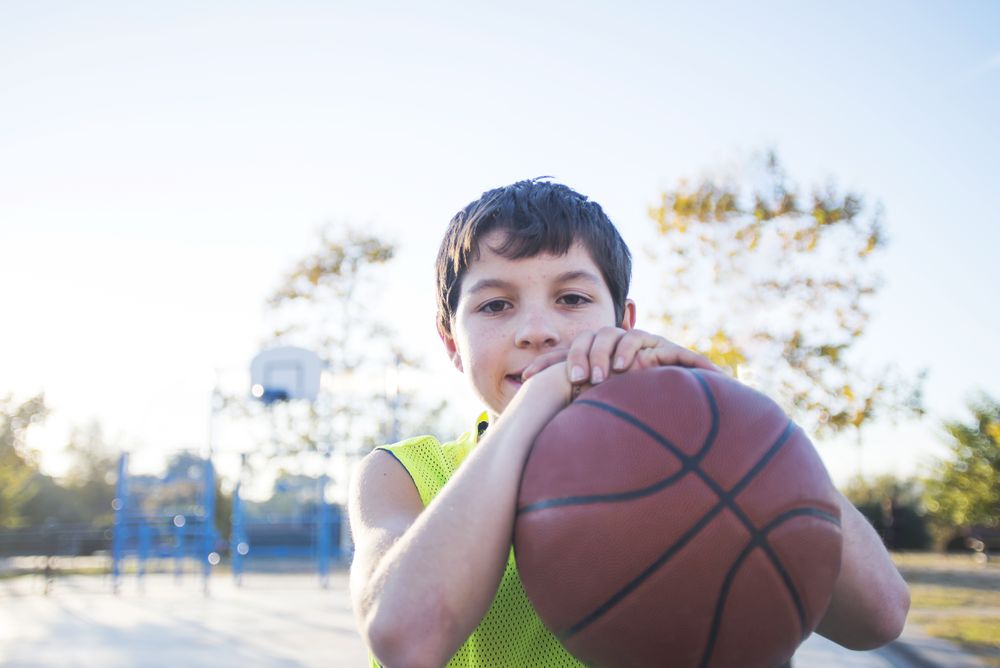 Portrait of a young teen male with sleeveless shirt standing on basketball court while smiling at camera