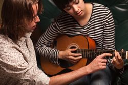 Young Male Musician Teaches Female Student To Play the Guitar