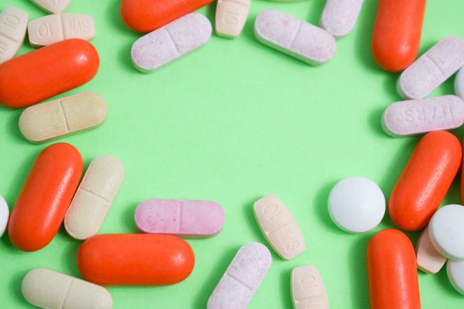 Pills and vitamins surrounding green background with copy space