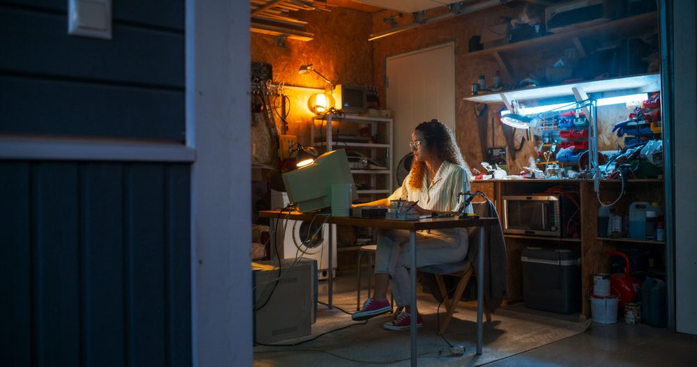 Wide Shot Of Hispanic Female Engineer Using Old Computer In Nineties Retro Garage In The Evening.