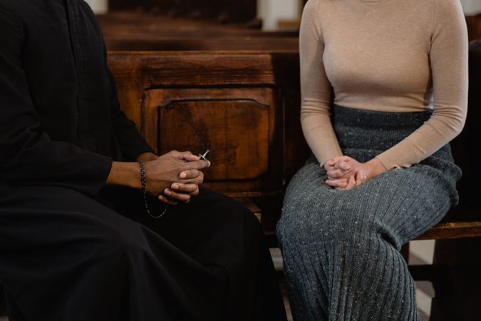 Cropped image of priest and woman in gray long skirt sittin indoor