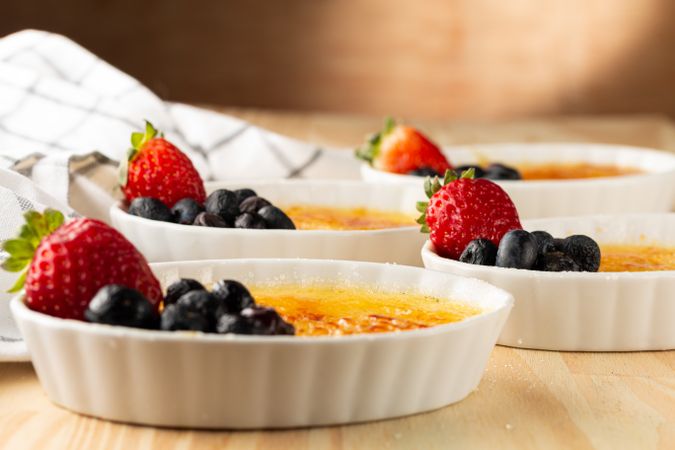 Side view of ramekins of creme brûlée with berries on wooden table