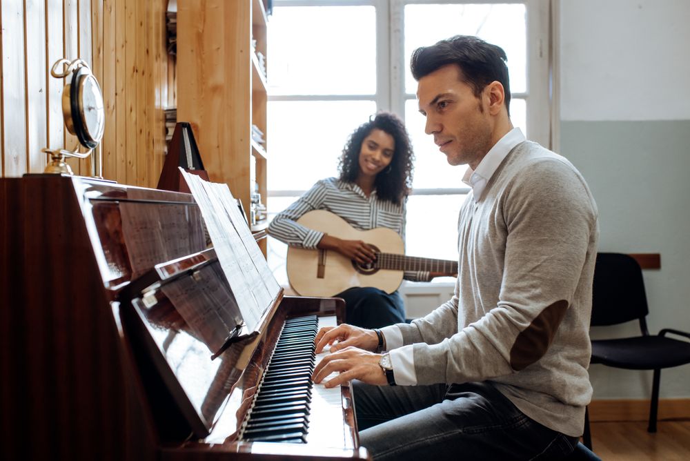 Man playing piano near woman playing guitar in studio