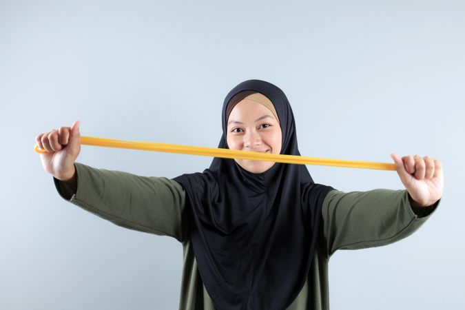 Young Asian Hijab Woman Stretching Yellow Resistance Band for Hand Pilates Exercise