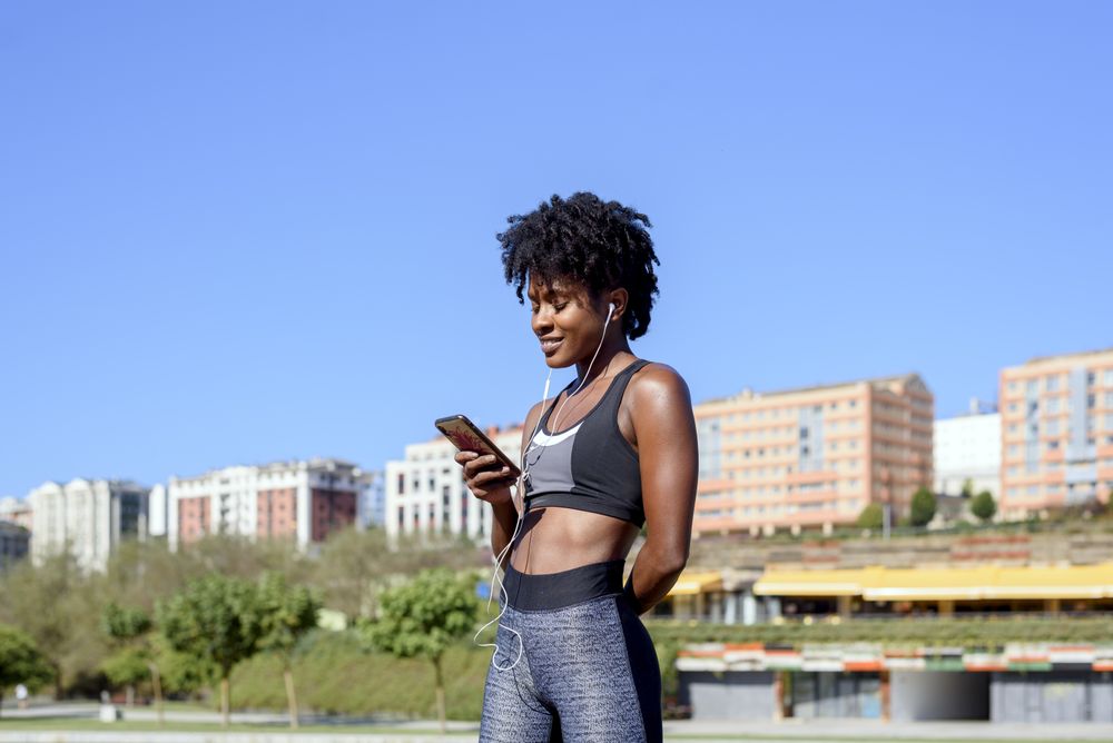 Cheerful Black sportswoman listening to music on smartphone