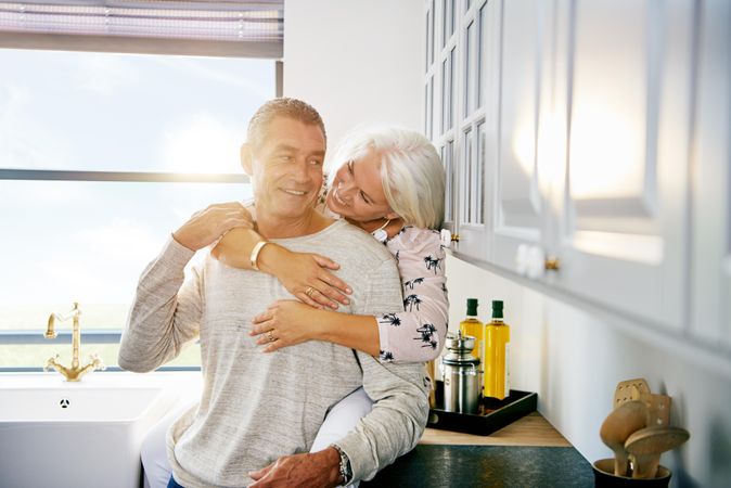 Happy mature woman holder her husband from behind in the kitchen