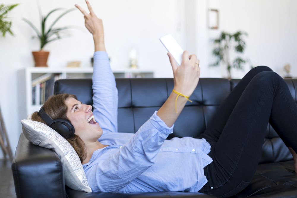 Excited woman lying on a sofa taking selfie on her phone