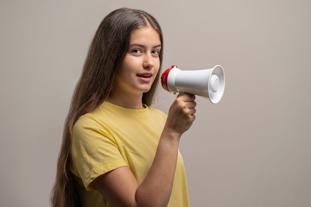 A young woman making an announcement with a megaphone on a studio background.
