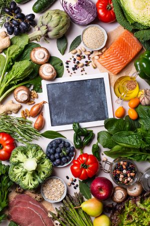 Flat lay of fresh vegetables, fruit and fish with chalk board