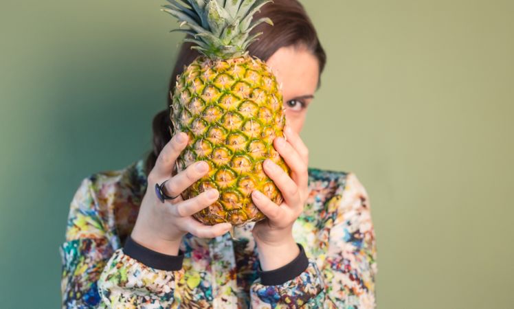 Woman holding pineapple in front of face