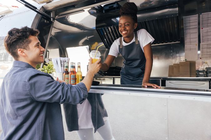 Food truck owner looking at customer as she passes him a drink