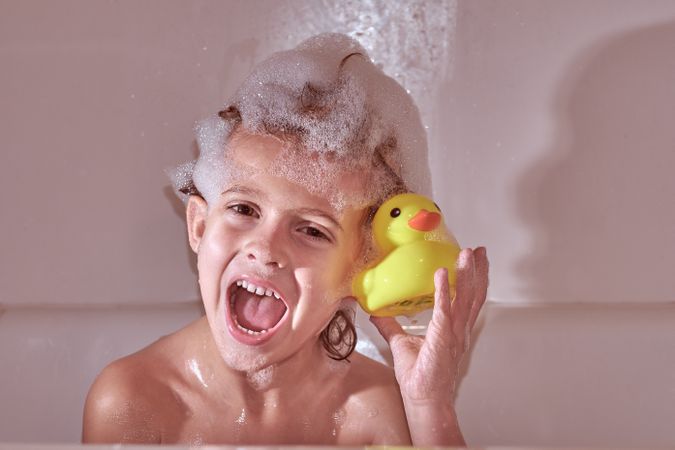 Happy boy with bath duck in bathtub