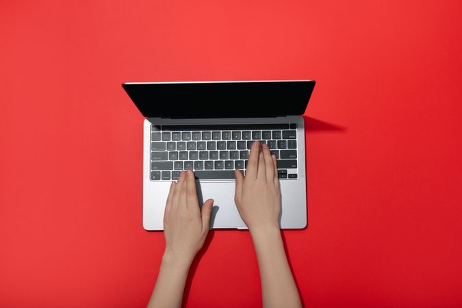 Top view of person typing on laptop keyboard on red table