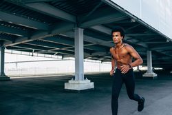 Black athletic male jogging under a bridge