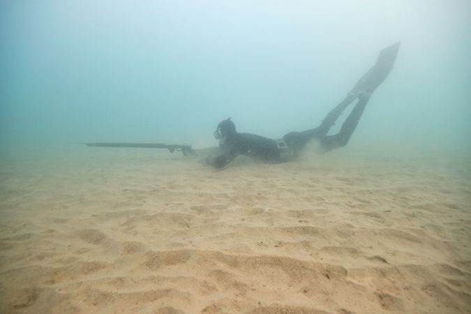 Underwater anonymous fisherman hunting near sandy bottom