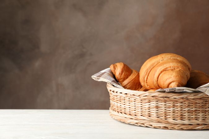 Wicker basket with croissants on table, copy space