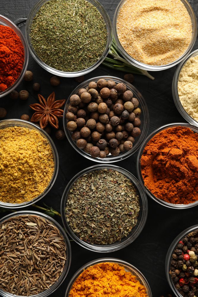 Vertical composition of glass bowls full of spices on dark table