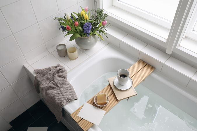 Top view of bathtub with foam, book, coffee and soap on a tray with fresh spring flowers