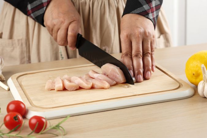 Female Hand Slicing Cut Chicken Fillet on Bamboo Chopping Board