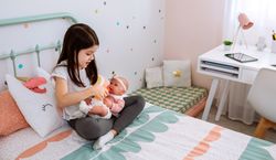 Little girl playing with her baby doll and leaving the tablet on the desk