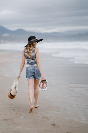 Young female walking barefoot on sandy beach