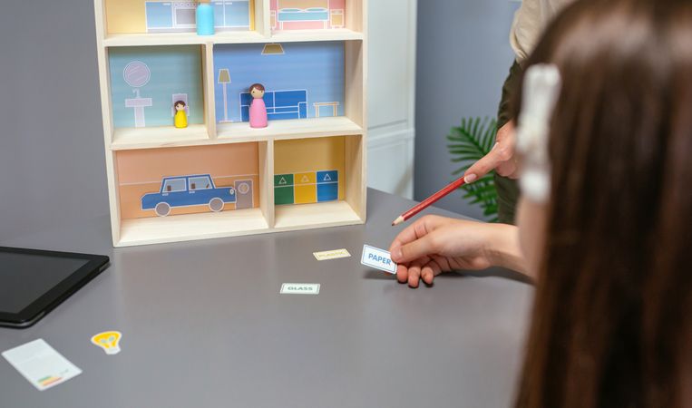 Unrecognizable teacher teaching recycling with a toy house to a female student in an ecology classroom