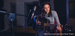 Female singer performing a song in studio and playing guitar 4AmO84