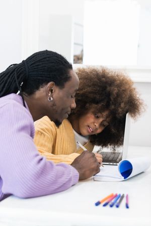 Black father helping daughter with homework on laptop