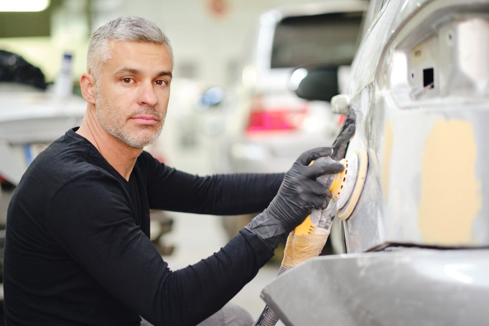 Mechanic grinding paint from car detail