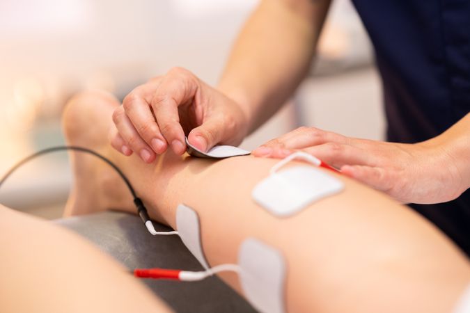 Physio placing electro pads for therapy on calf muscle of patient