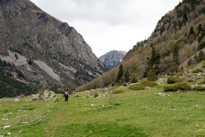 Unrecognizable traveling woman in green valley near mountains