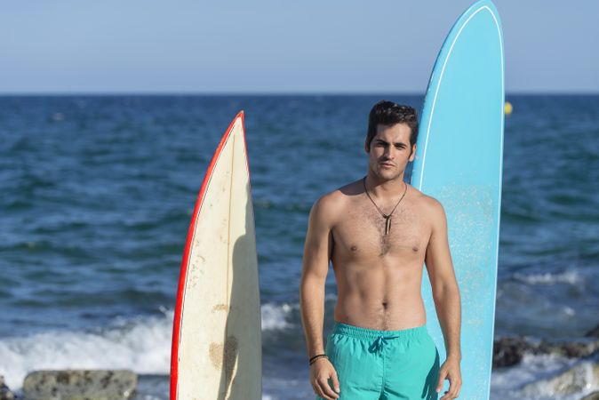 Male surfer standing with boards in front of the water