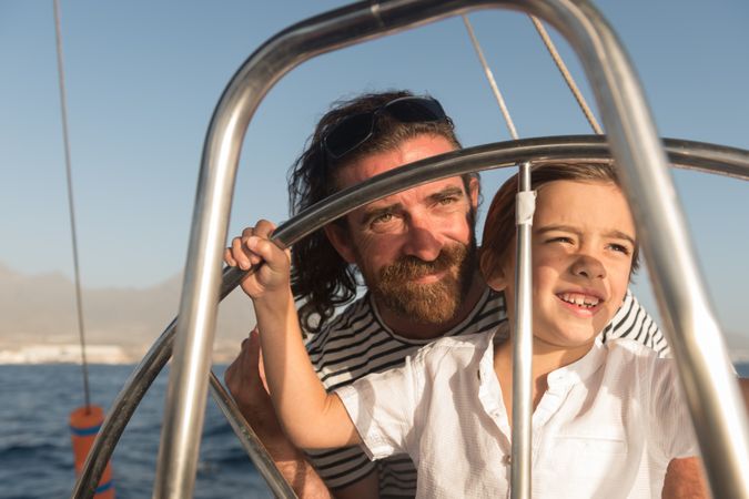 Man with boy holding steering wheel on yacht on water
