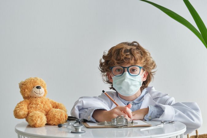 Boy in medical uniform with toy bear during checkup