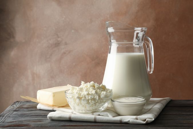 Milk, cottage cheese and butter on wooden table against brown background