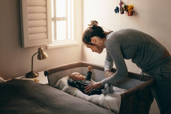 Mother putting her baby to sleep on a bedside baby crib
