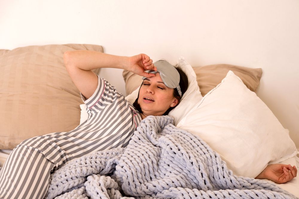 Woman waking up, adjusting eye mask in bed.