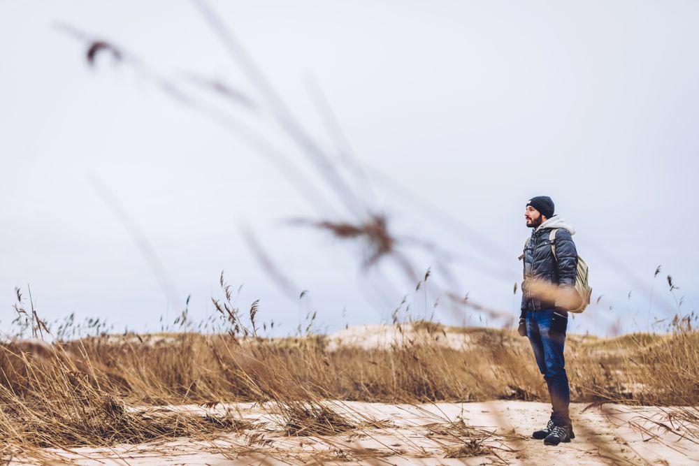 Man walking between sand field with dry grass