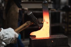 Blacksmiths forging hot metal with hammer in workshop