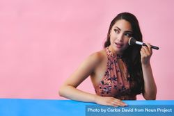 Surprised Hispanic woman with long brown hair holding large make up brush, copy space 0PR2l4