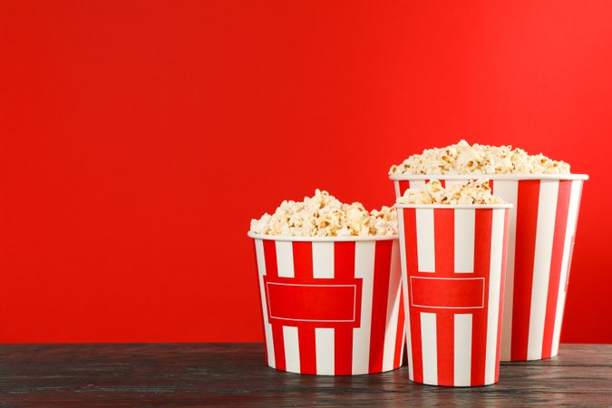 Striped buckets with popcorn against red background, space for text