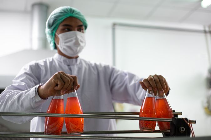 A factory worker is picking up a bottle of fruit juice from a moving conveyor belt inside a beverage production facility.