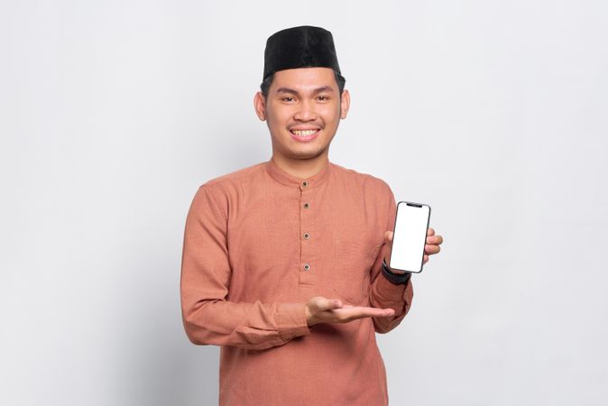Muslim man in kufi hat smiling and presenting light screen on mobile phone